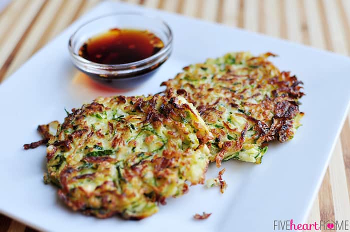 Zucchini Fritters ~ these golden, delicious fritters are crispy on the outside, creamy on the inside, and accompanied by a sweet and salty, Asian-inspired dipping sauce! | FiveHeartHome.com two fritters on a square plate with sauce