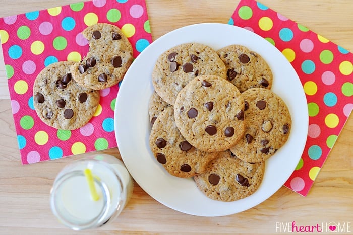 Aerial shot of chocolate chip cookies on a plate with milk and colorful napkins.