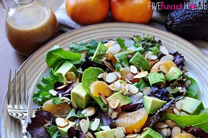 Salad on a plate topped with mandarins, almonds, avocado, and Sesame Ginger Vinaigrette.