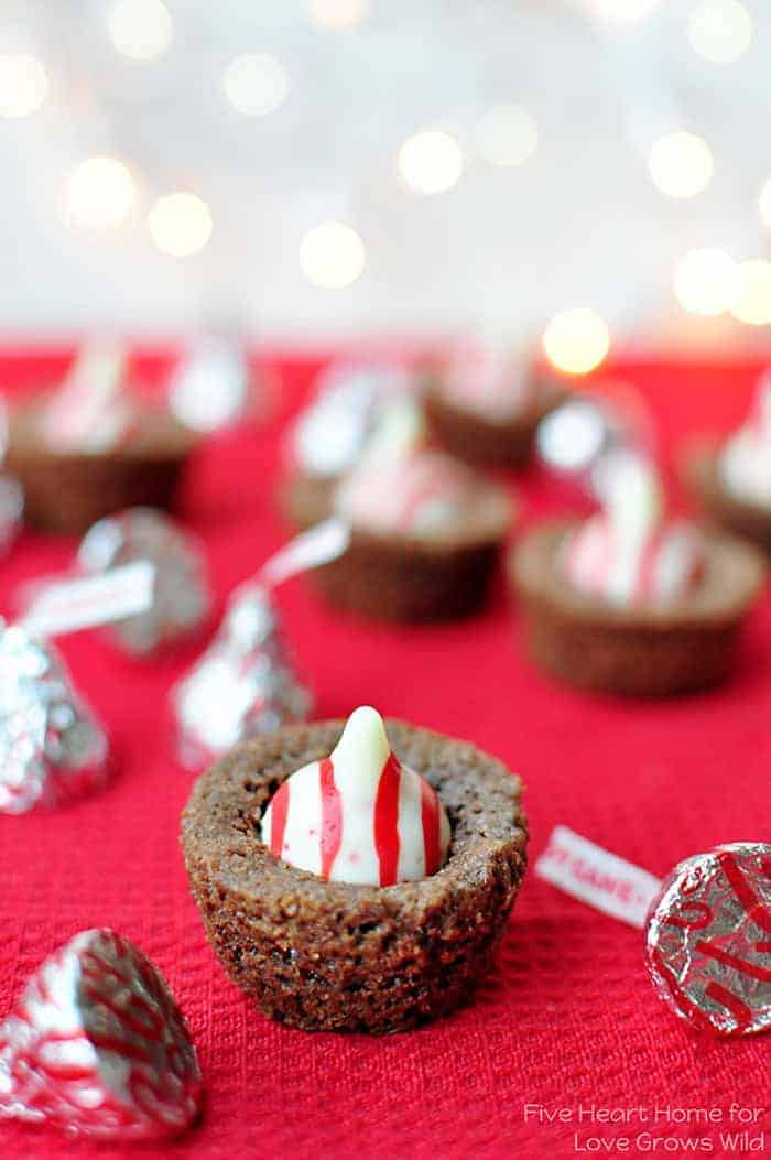 Christmas Brownie Bites on a red cloth with Candy Cane Hershey's Kisses sprinkled on table and twinkle lights in the background