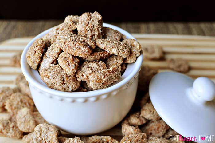 Bowl with lid containing Cinnamon Sugar Pecans, plus more spilled on table.