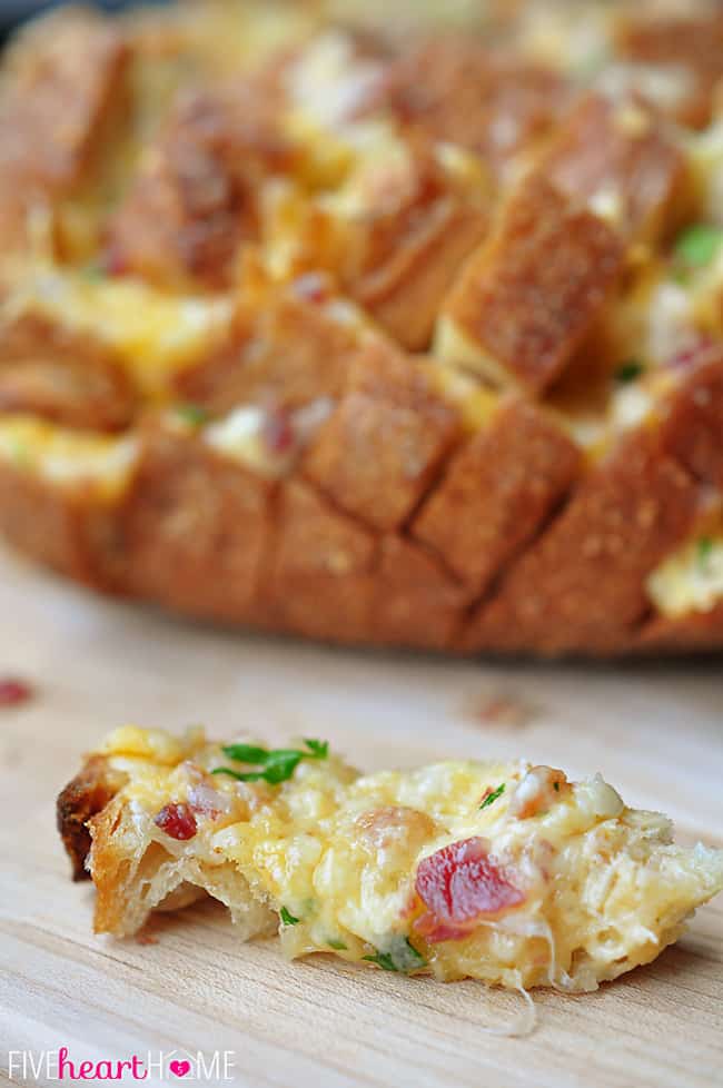 Piece of Cheesy Pull-Apart Bread with Bacon, Garlic, Cheddar and Swiss, laying on wooden board.