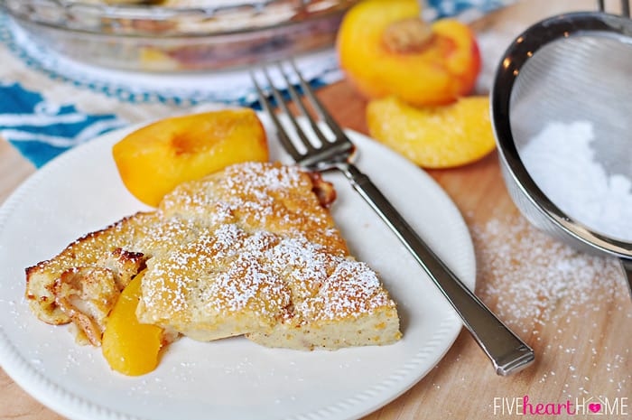 Peach German Pancake (Dutch Baby) ~ golden, puffy, and piping hot skillet pancake studded with peaches | FiveHeartHome.com Serving on white plate with powdered sugar and fresh peaches on the side.