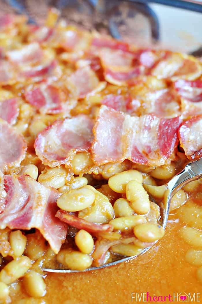 Easy Southern Baked Beans ~ this sweet and savory side dish is topped with bacon, and it's quick to whip up using canned white beans | FiveHeartHome.com Close-up with big scoop being removed with bacon all over surface.