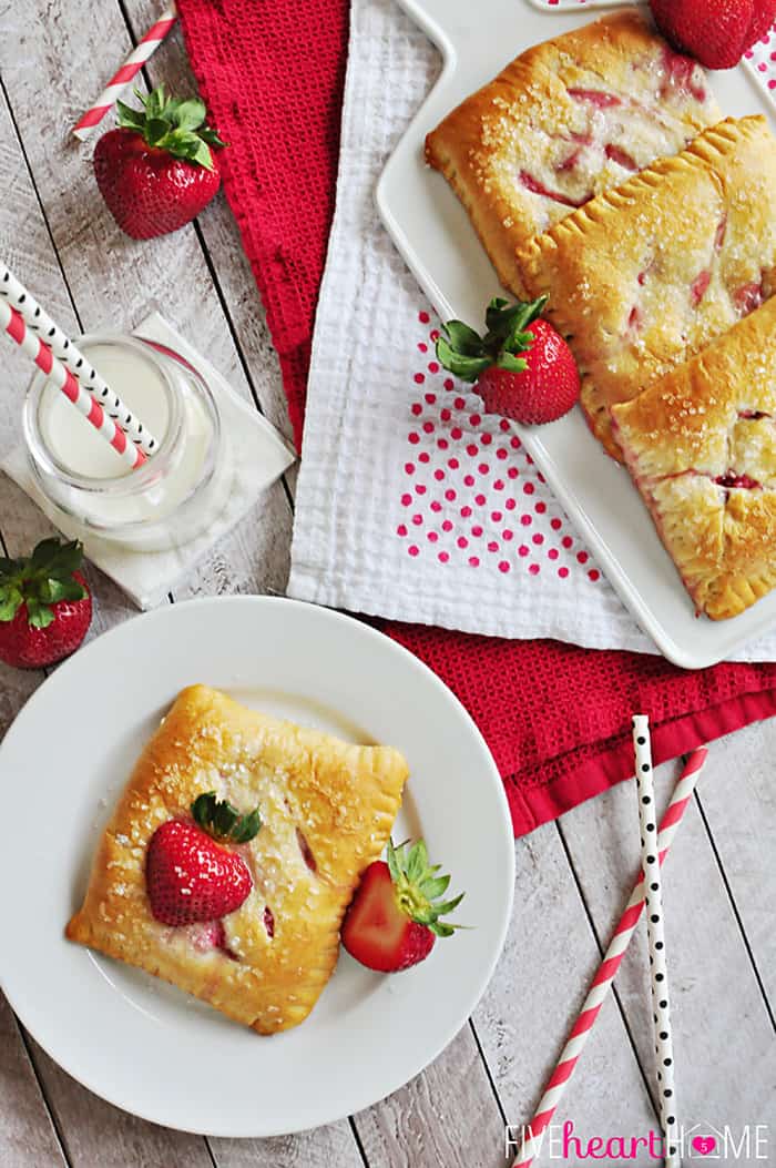 Easy Strawberry Pastries ~ these scrumptious breakfast treats are quick and easy to make with crescent roll dough, cream cheese filling, and fresh sliced strawberries! | FiveHeartHome.com Aerial view of plate and platter of Strawberry Pastries, with glass of milk and fresh strawberries on table.