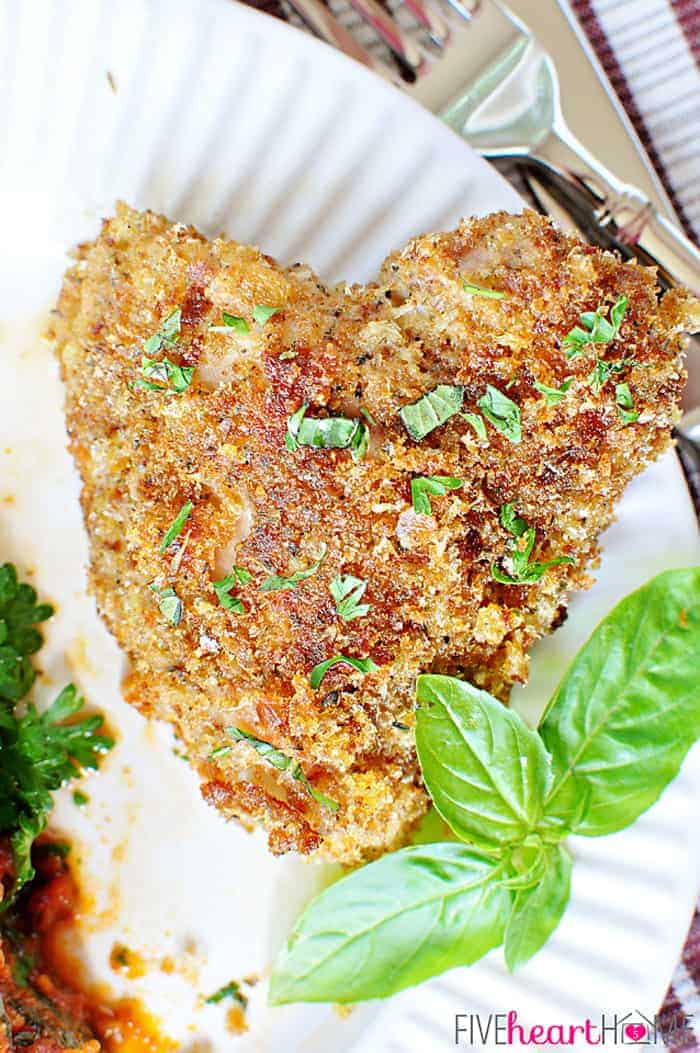 Heart-shaped piece of Baked Italian Chicken on a plate with fresh basil.