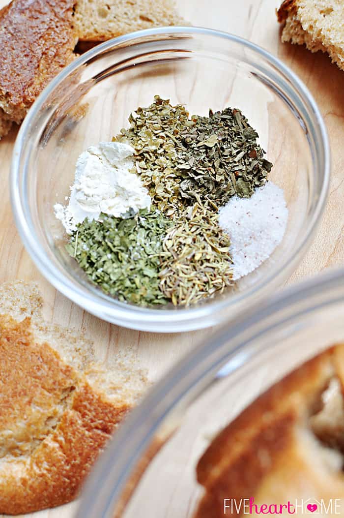 Bowl of herbs and spices and pieces of dried bread on table.