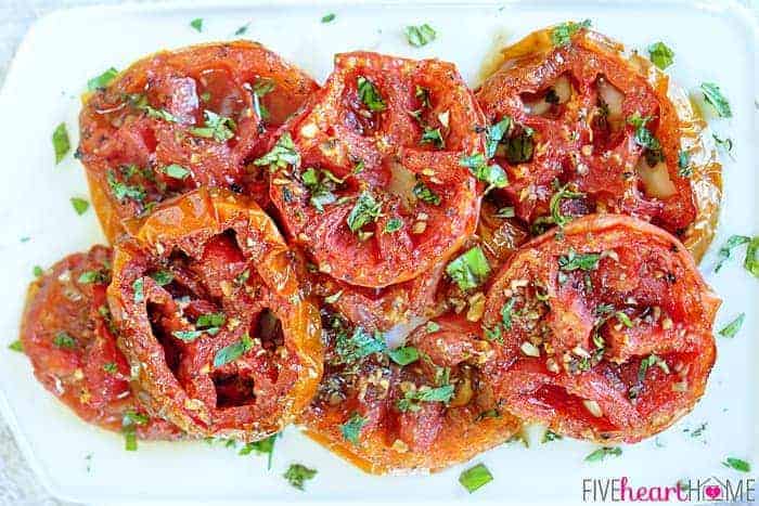 Aerial view of Oven Roasted Tomatoes on a white platter with fresh herbs.