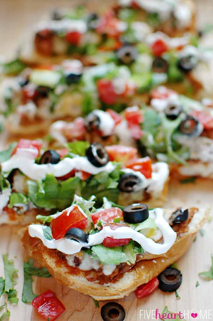 French Bread Taco Pizza Sliced on a Cutting Board with All the Fixings 