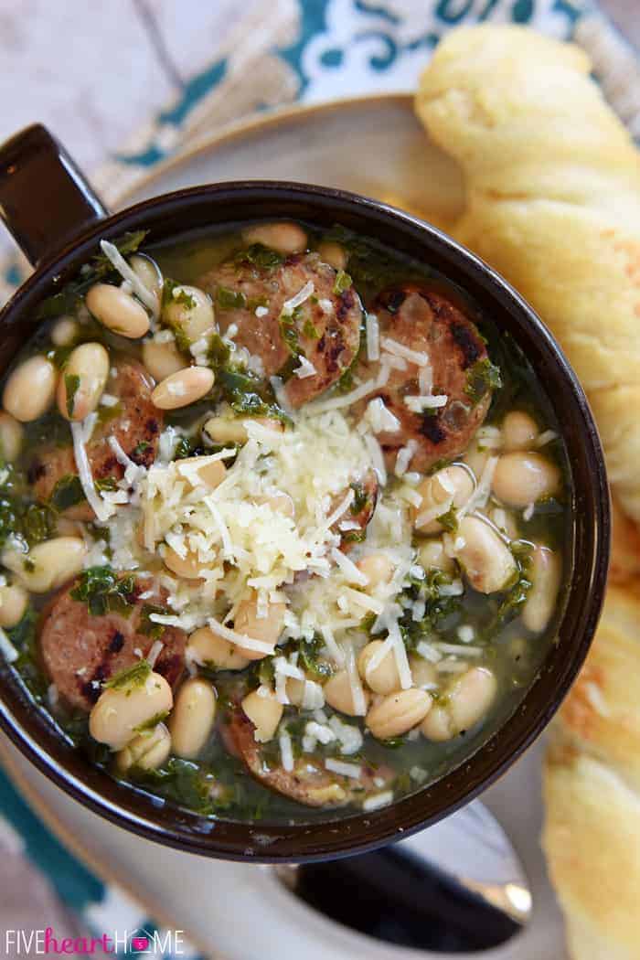 Close-up of soup showing sausage, white beans, kale, and parmesan cheese.