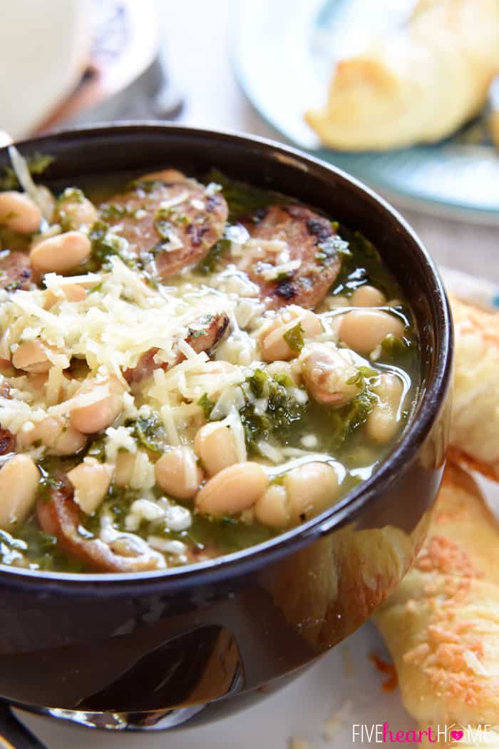 Sausage Kale White Bean Soup in brown bowl with breadsticks on side.