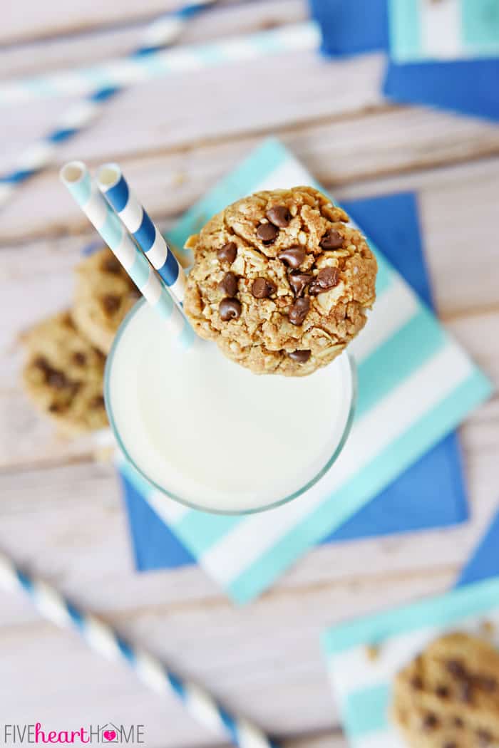 Breakfast Cookie resting on edge of glass of milk with blue and white paper straws.