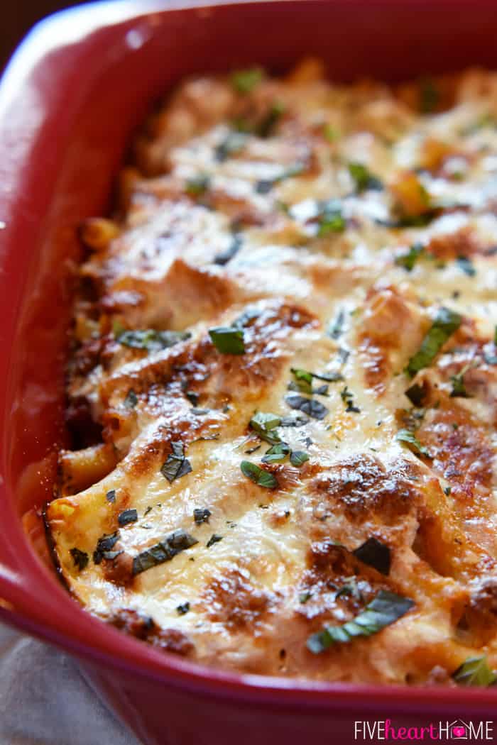 Baked Ziti ~ easy to make and oozing with cheese, this pasta dish is comfort food perfection! | FiveHeartHome.com Fresh From the Oven with Basil Garnish and Cheesy Topping in Red Baking Dish