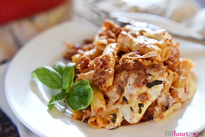 Baked Ziti ~ easy to make and oozing with cheese, this pasta dish is comfort food perfection! | FiveHeartHome.com Pasta Oozing With Cheese Served on a White Plate with Fresh Basil Sprig