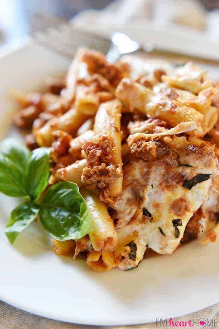 Baked Ziti ~ easy to make and oozing with cheese, this pasta dish is comfort food perfection! | FiveHeartHome.com Baked Ziti Served on White Plate with Fresh Basil Sprig for Garnish