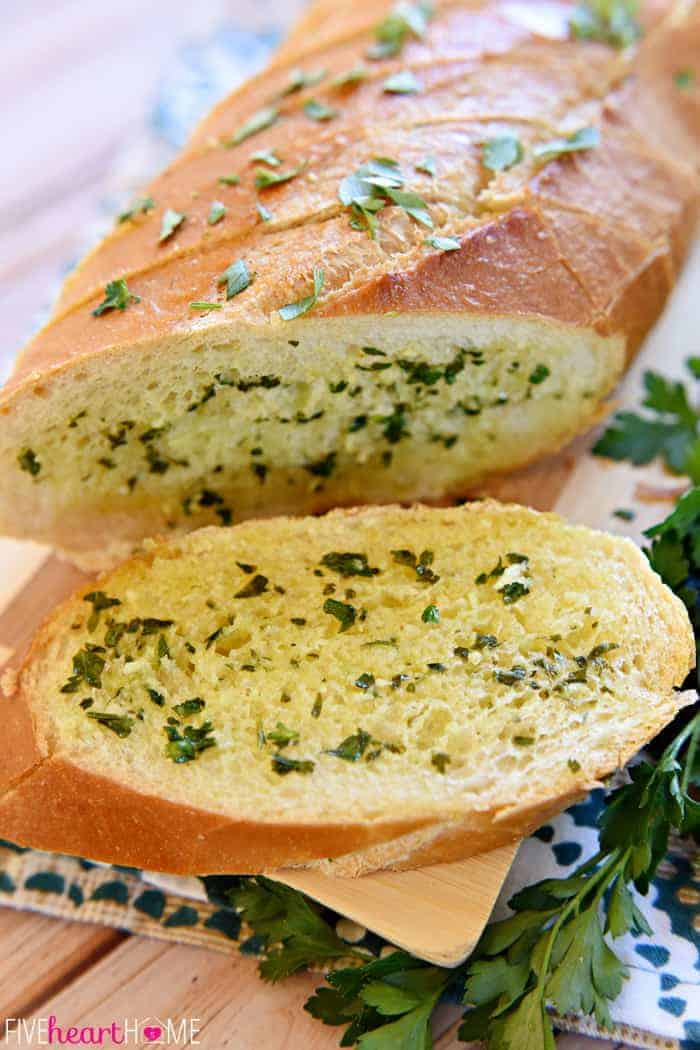 Slice of Garlic Bread with Fresh Garlic and Parsley on Decorative Tea Towel 