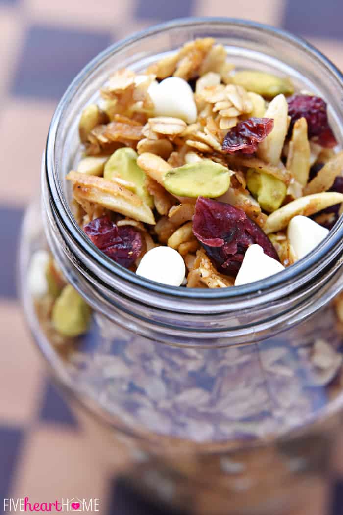 Glass jar of Gingerbread Granola showing cranberries, pistachios, and white chocolate chips.