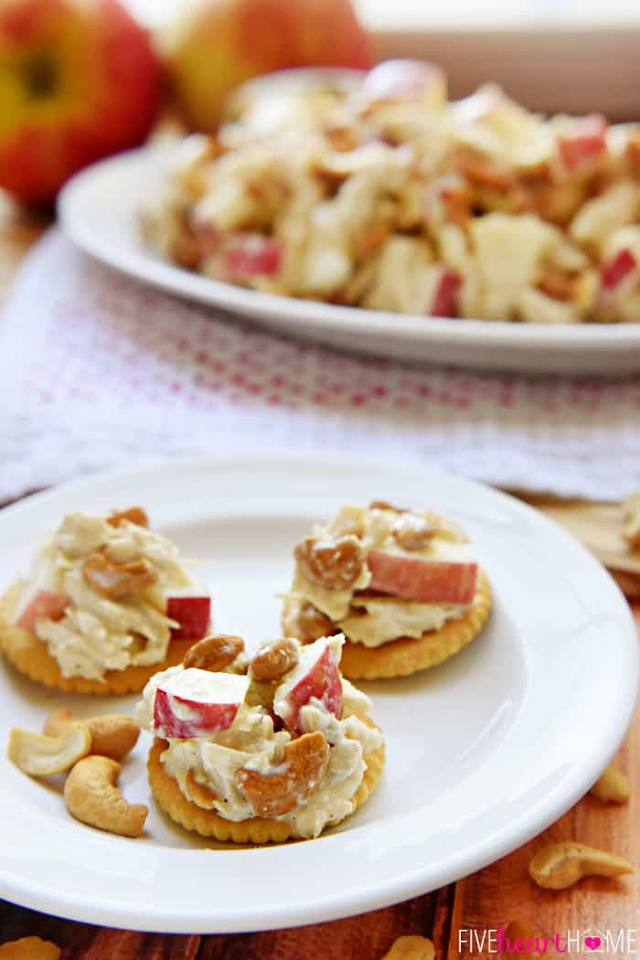 Three topped crackers on a plate, plus a platter of Chicken Salad with Apples in the background.