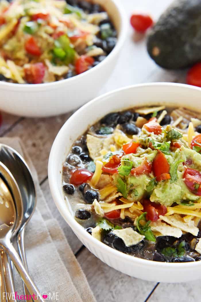 Bowls of Chicken Black Bean Soup with a stack of spoons and an avocado in the background