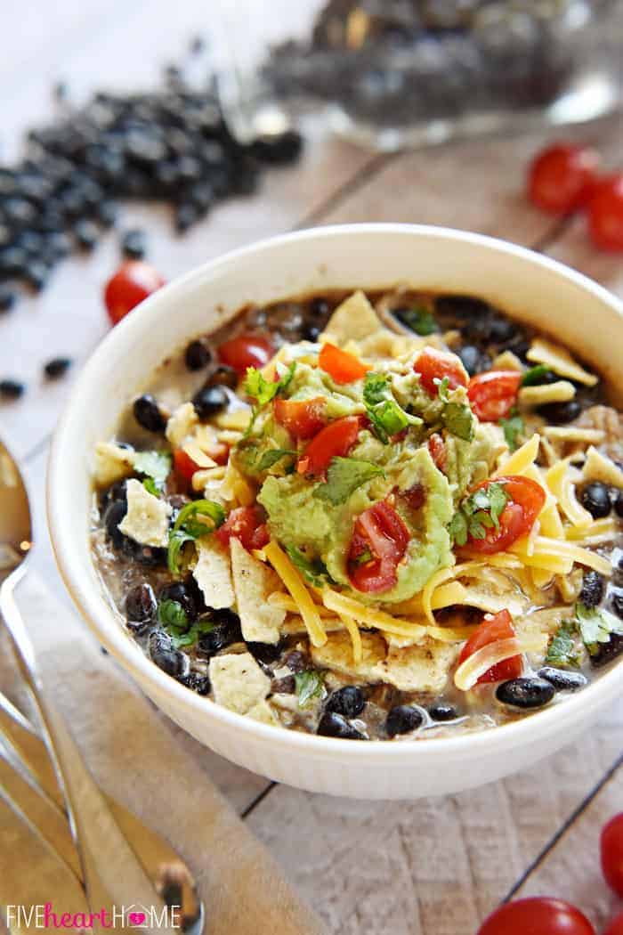 Black bean soup in a white bowl with toppings of chips, avocado, tomatoes, cheese and cilantro