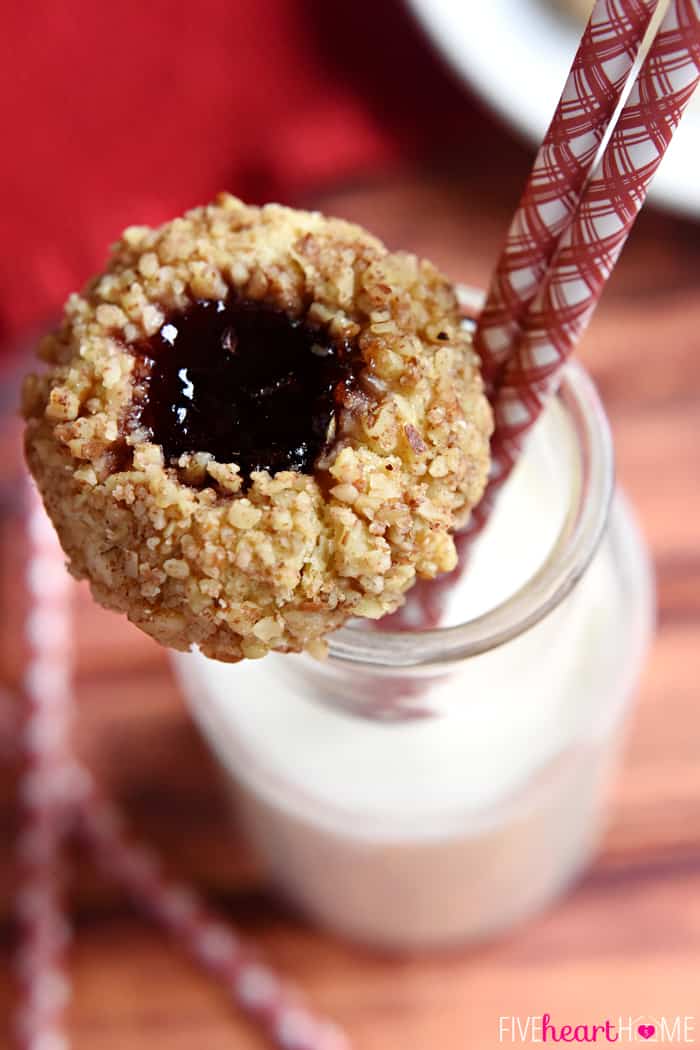 Thumbprint Cookie resting on the rim of a jar of milk with two paper staws.