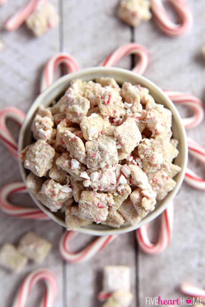 Aerial view of Christmas Puppy Chow in a white bowl surrounded by candy canes.