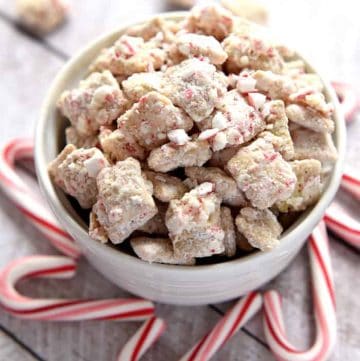 Christmas Puppy Chow in a bowl surrounded by candy canes.