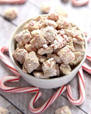 Christmas Puppy Chow in a bowl surrounded by candy canes.