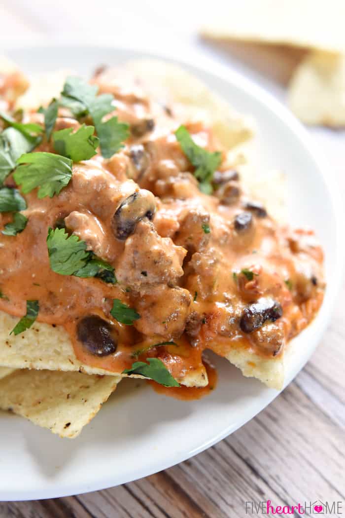 All-Natural Chili Cheese Dip Poured on Top of a Pile of Tortilla Chips on A White Platter 