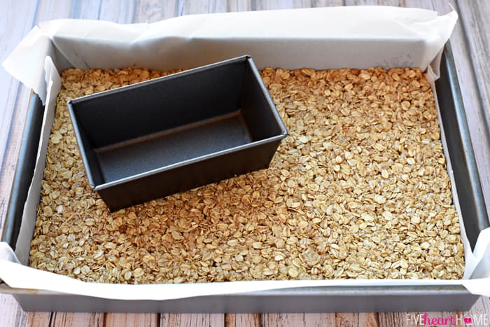 Demonstrando como pressionar para baixo a mistura de barra de granola usando uma pequena forma de pão