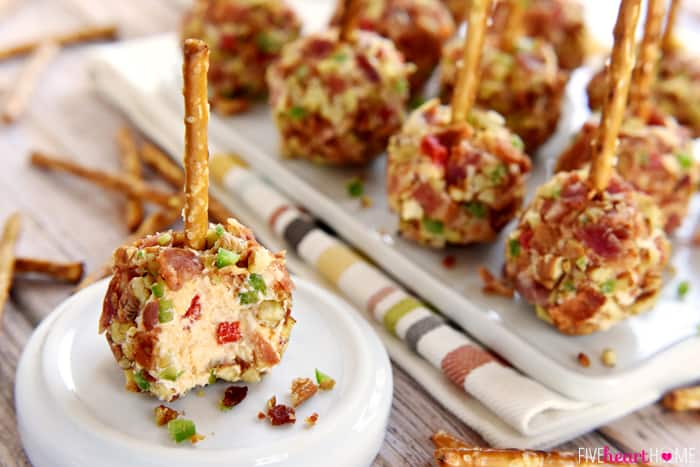 Pimento Cheese and Bacon Mini Cheese Ball Bites ~ mini cheese balls of homemade pimento cheese are rolled in a coating of crispy bacon, toasted pecans, and minced fresh jalapeños and then speared with a pretzel stick for fun, easy-to-eat appetizers, perfect for game day or any get-together! | FiveHeartHome.com Pimento Cheese and Bacon Mini Cheese Balls on plate and platter.