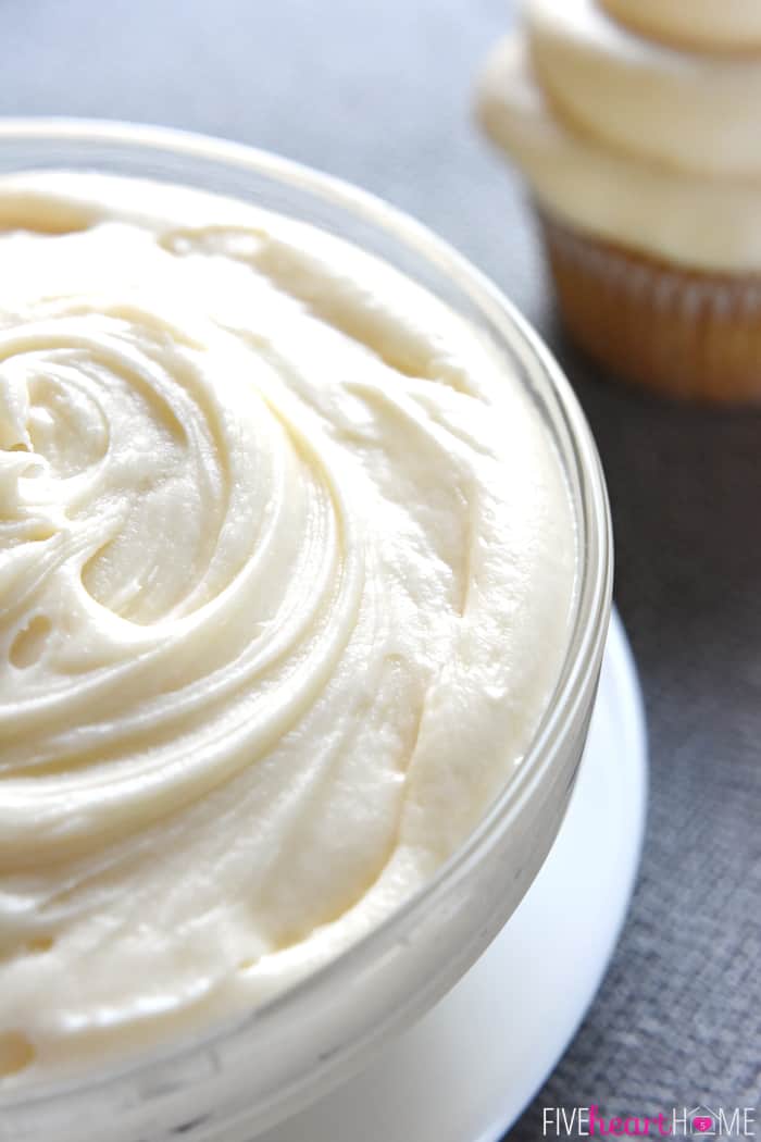 Close-up of a bowl of Cream Cheese Frosting with frosted cupcake in the background.