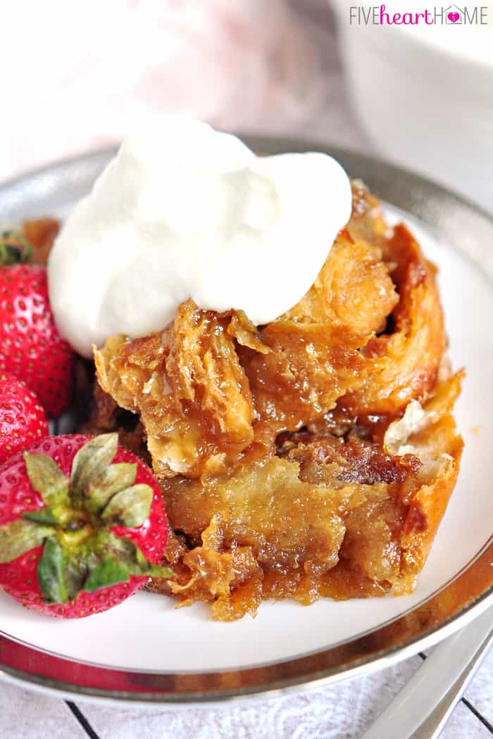 Easy Caramel Croissant Bread Pudding on Silver Rimmed Plate with Fresh Strawberries and Whipped Cream 