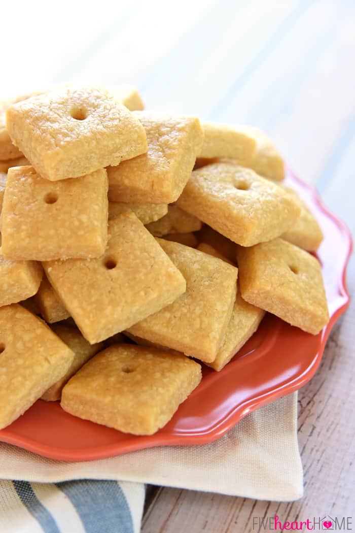 Homemade Cheese Crackers ~ tasty and all-natural, these savory crackers are not only kid approved, but you won't believe how easy they are to make! | FiveHeartHome.com Cheese crackers piled onto bright orange plate.