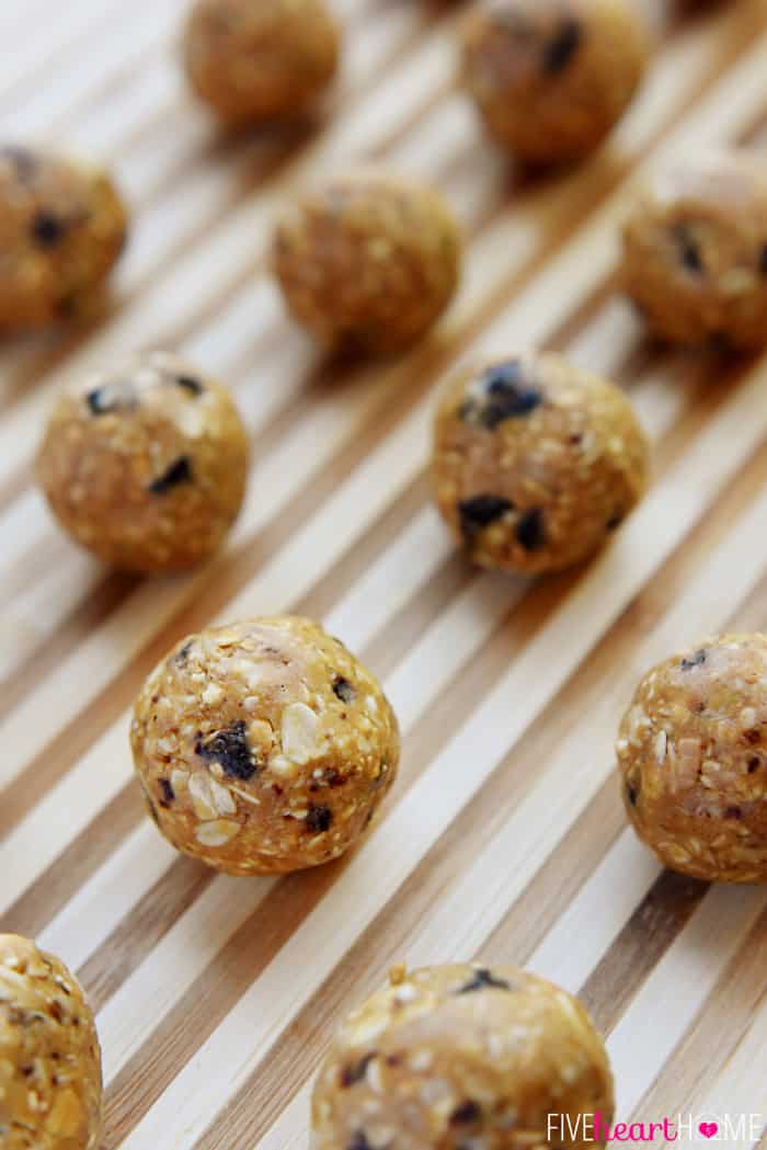 Oatmeal Cookie Energy Bites ~ tasty, no-bake balls combining oats, ground nuts, dried fruit, nut butter, and honey...perfect as a portable breakfast-on-the-go, a protein-packed snack, or a no-guilt-necessary sweet treat! | FiveHeartHome.com Oatmeal Energy Bites lined up on striped board.