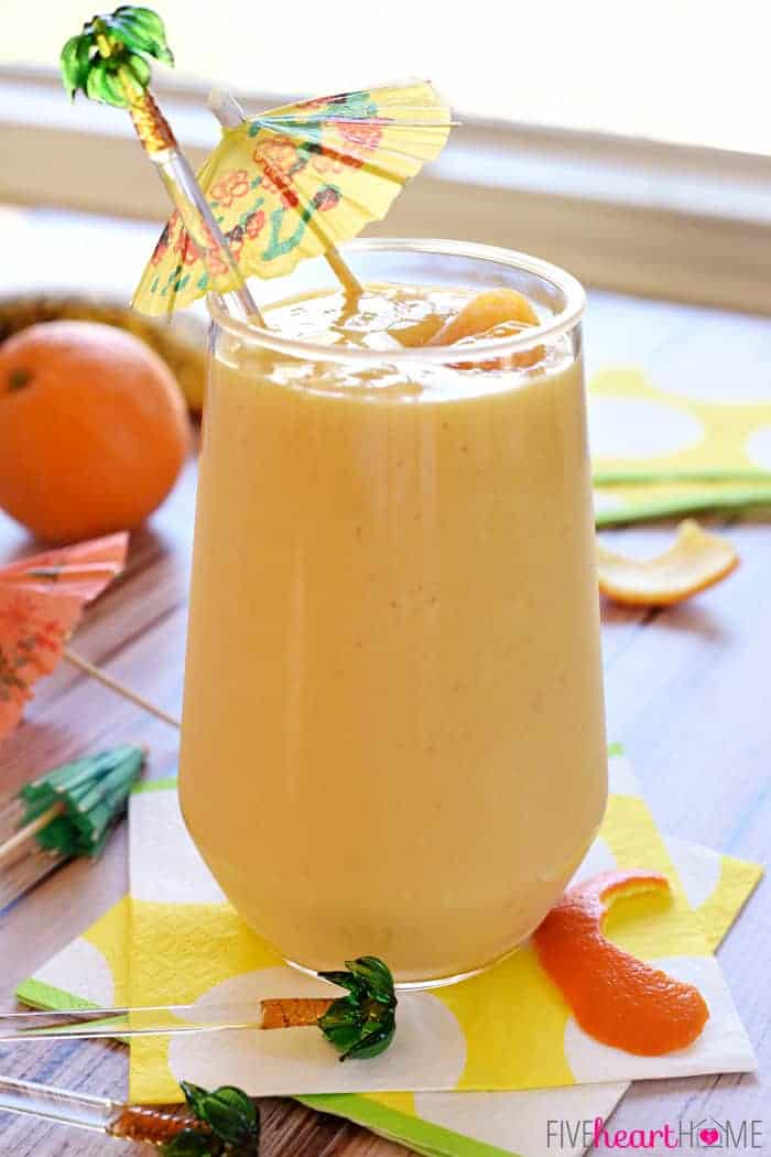 Sunshine Smoothie in a tall glass garnished with a palm tree pick and mini umbrella.