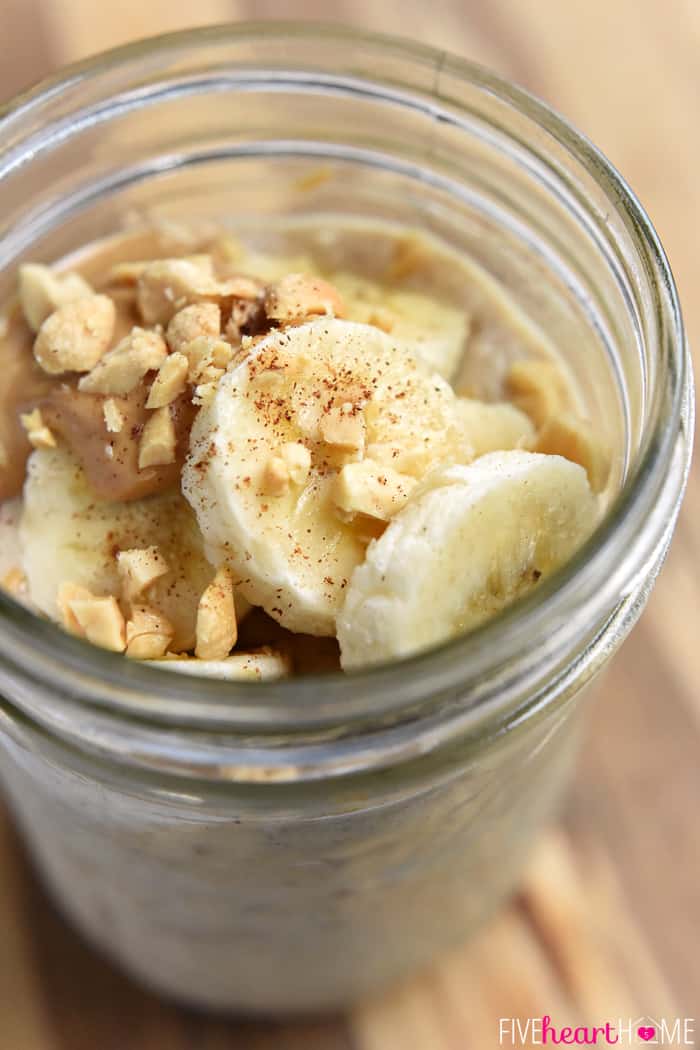 Close-up of jar topped with sliced bananas, peanut butter, and chopped peanuts.