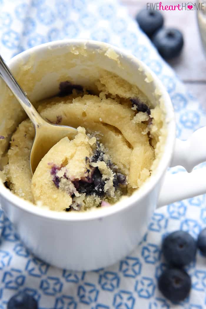 Blueberry Muffin Mug Cake with with spoon and fresh berries.