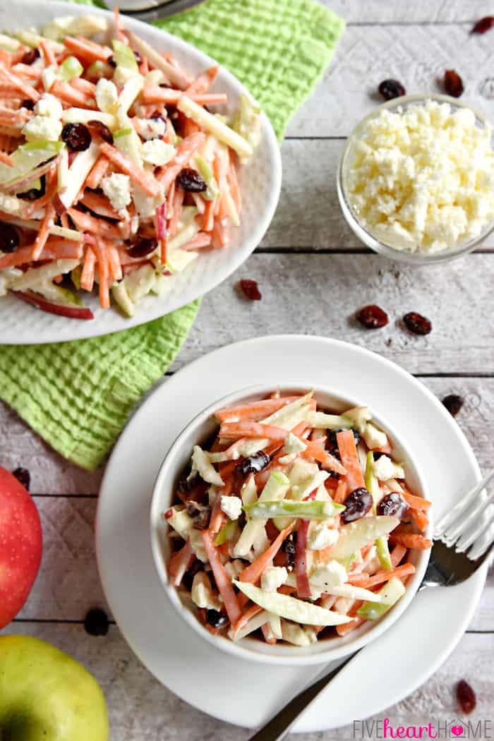 Aerial view of Carrot Apple Slaw on serving platter and in bowl with feta and cranberries on table.