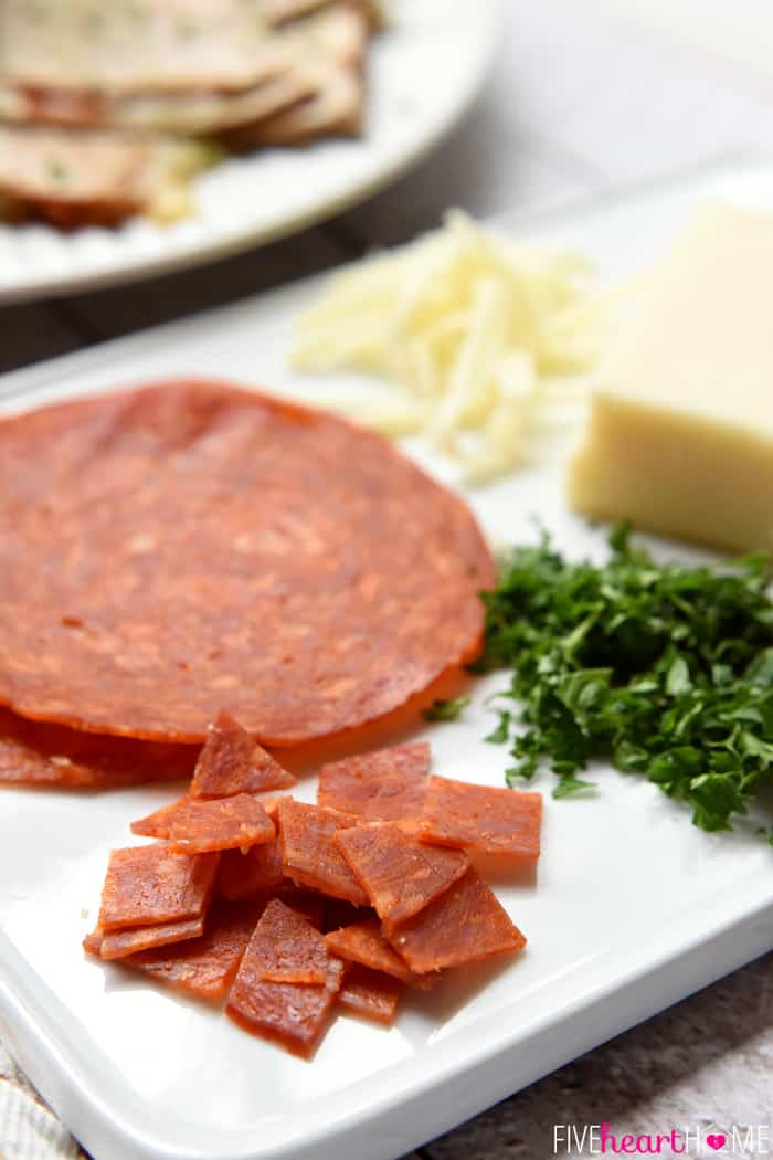 White board of ingredients including diced and whole pepperoni, grated mozzarella, and minced herbs