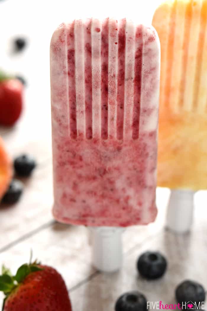 Yogurt Popsicles standing upright on table surrounded by fruit.