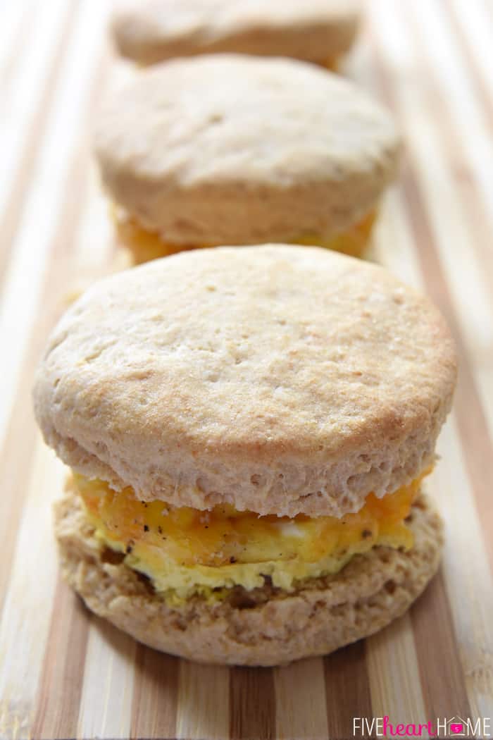 Easy Freezer Breakfast Sandwiches ~ cheesy scrambled eggs with ham are sandwiched inside of flaky biscuits in these make-ahead sandwiches that freeze beautifully...perfect for busy mornings and breakfast on-the-go! | FiveHeartHome.com Frozen Breakfast Sandwiches lined up on cutting board.