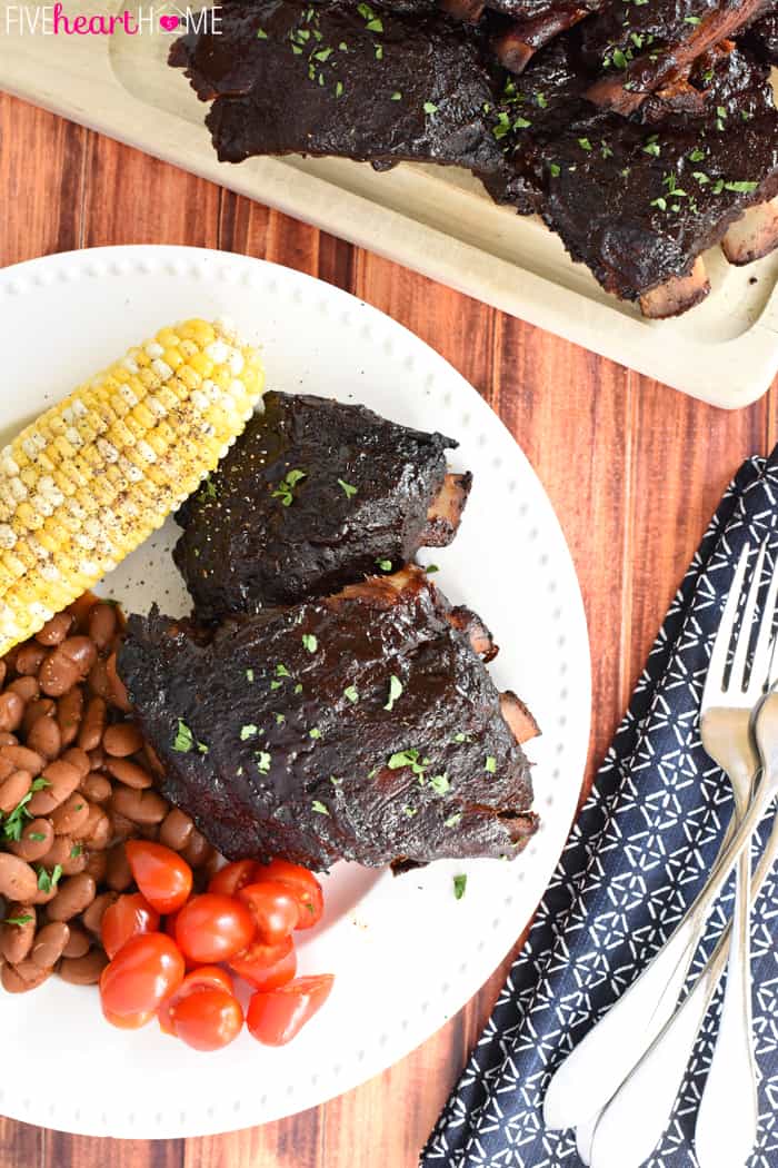 Aerial view of cutting board of crock pot ribs, loaded plate, napkin, and silverware