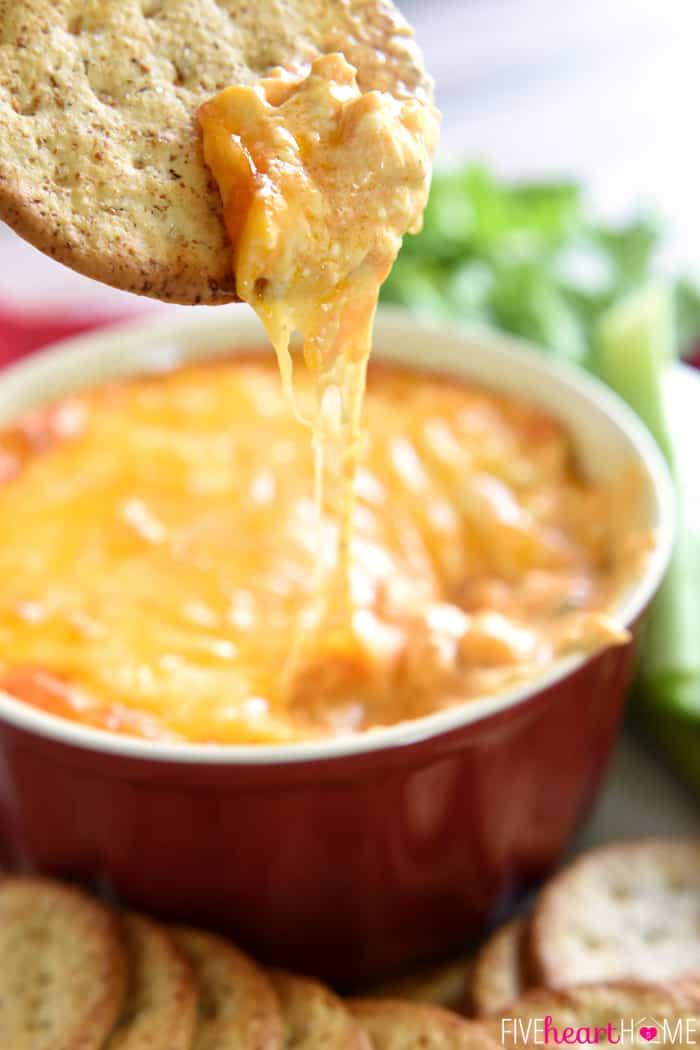 Buffalo Wing Dip (AKA, Buffalo Chicken Dip) ~ warm, creamy, and loaded with cheese, chicken, and wing sauce, this decadent appetizer is perfect for parties or ideal for game day tailgating! | FiveHeartHome.com Chicken Wing Dip recipe on cracker with bowl of Buffalo Chicken Dip in background.