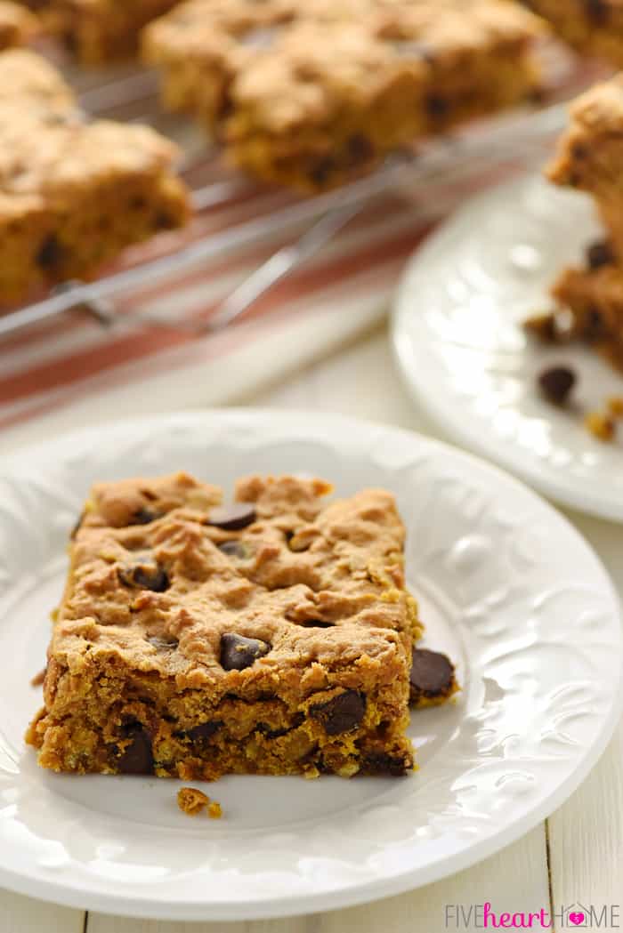 Chewy Pumpkin Chocolate Chip Oatmeal Bars ~ soft, moist, and loaded with pumpkin, chewy oats, warm spices, and rich chocolate chips for a perfect fall treat! | FiveHeartHome.com Single cookie bar on a plate with more Pumpkin Chocolate Chip Bars on a cooling rack in the background