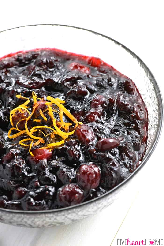 Cranberry Cherry Sauce in a decorative glass bowl garnished with orange zest.