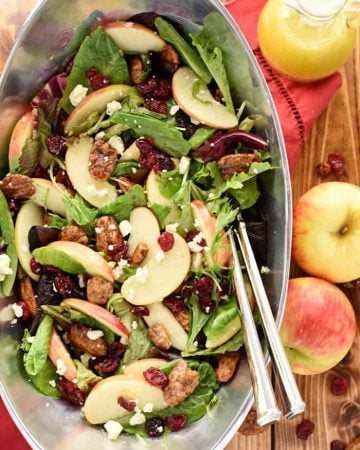 Aerial view of Holiday Honeycrisp Salad in pewter bowl with apples and dressing on table.