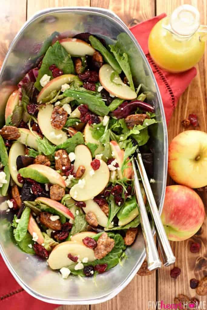 Aerial view of Holiday Honeycrisp Salad in pewter bowl with apples and dressing on table.