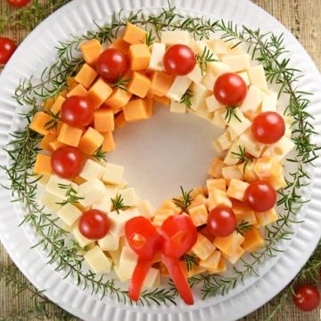 Holiday Cheese Wreath ~ this easy and festive Christmas party appetizer is made by arranging cubes of cheese in a ring, accenting with cherry tomatoes and a garland of rosemary, and finishing off with a bell pepper bow! | FIveHeartHome.com