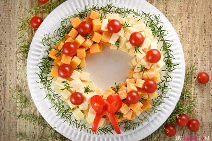 Holiday Cheese Wreath ~ this easy and festive Christmas party appetizer is made by arranging cubes of cheese in a ring, accenting with cherry tomatoes and a garland of rosemary, and finishing off with a bell pepper bow! | FIveHeartHome.com
